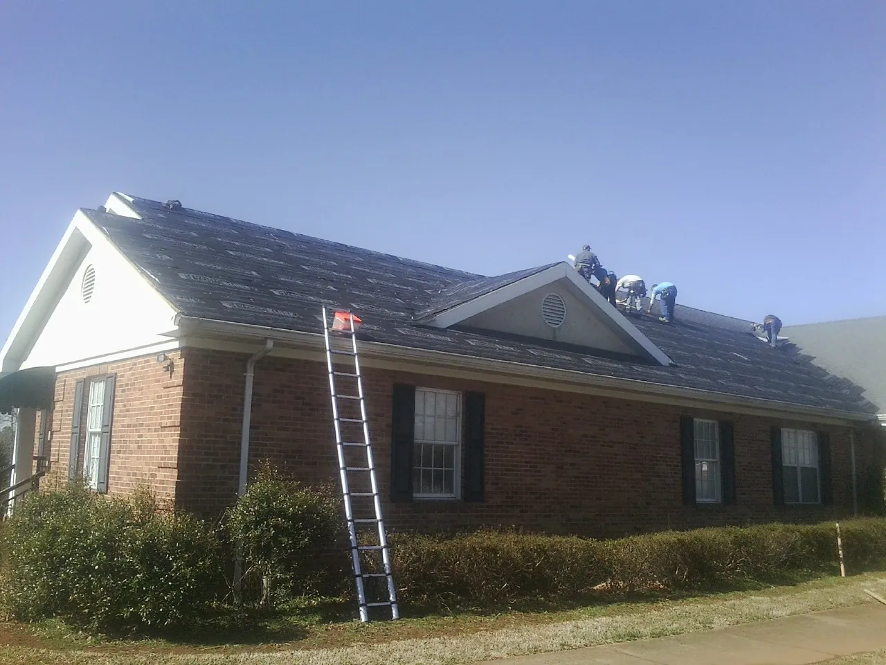 Crew tearing shingles off a brick ranch roof with a ladder set — Metal Roof Repair work by our crew in Pleasanton